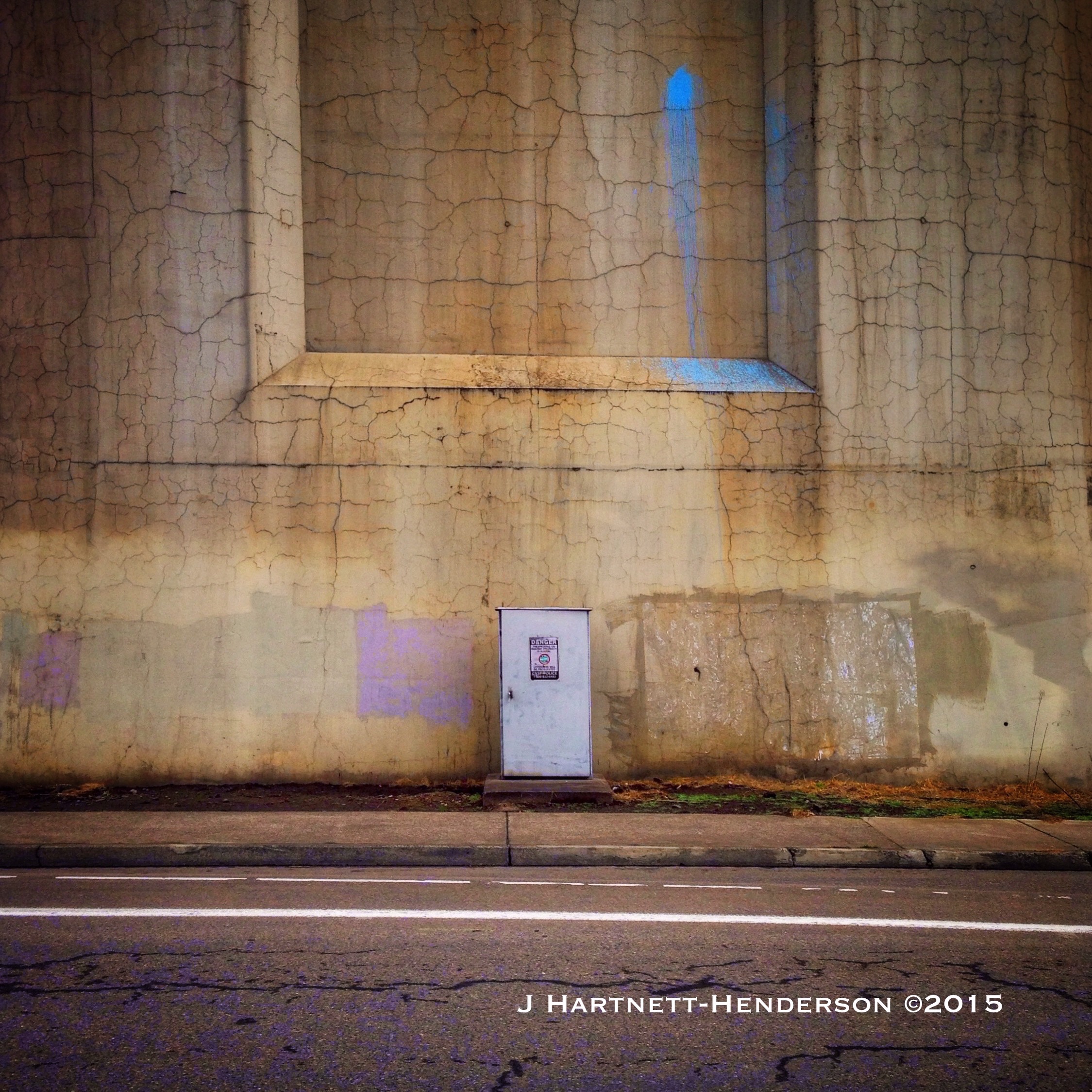 Cracked bridge support column with a splash of blue paint spatter and painted over graffiti
