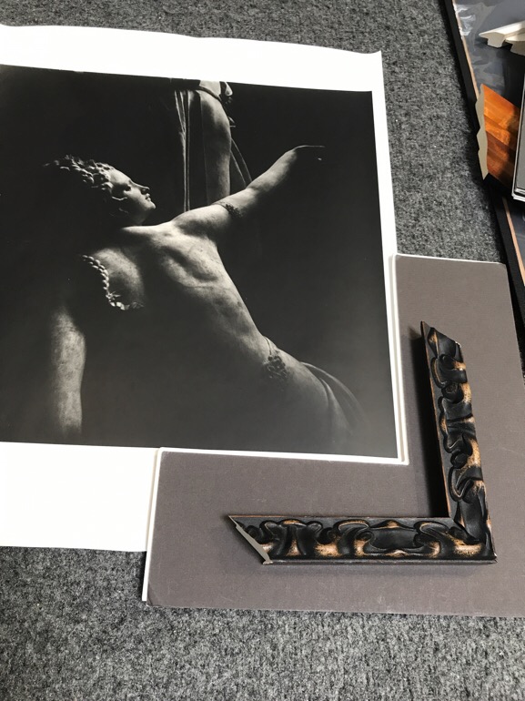 A black and white photograph of a stone sculpture of a woman with braided hair and a frame that has raised art noveau shapes