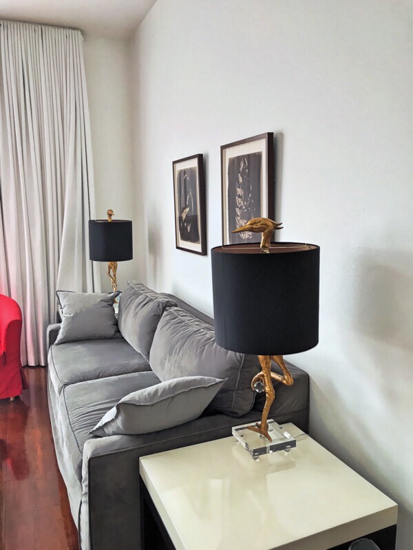 Framed chocolate brown Van Dyke prints hang above a medium gray sofa flanked by gold bird lamps