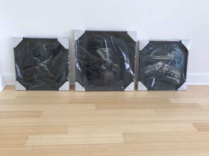 The three black and white photographs framed and wrapped in plastic ready to be installed.