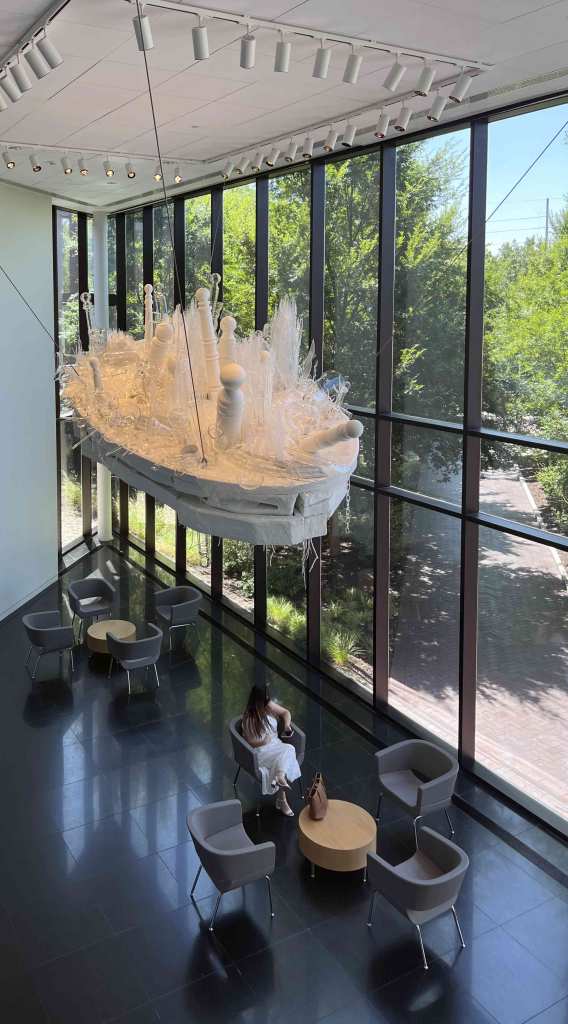 white boat shape loaded with glass shards and shapes hangs from the ceiling of the foyer of the Wichita Art Museum threatening visitors with an untimely crash
