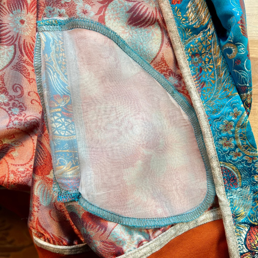 Close-up view of the interior of a jacket showcasing the pocket made of silk organza against a colorful brocade fabric.